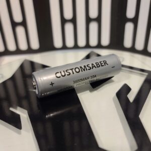 A silver cylindrical object labeled CUSTOMSABER on a black surface.