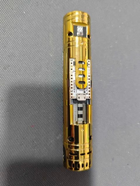 Close-up of a gold vape pen with a visible gauge and button.