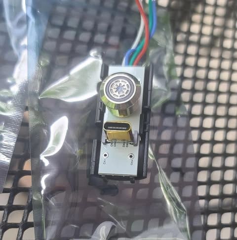 Small electronic camera module with multi-colored wires on a grid surface.